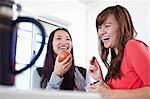Two young women in kitchen eating fruit