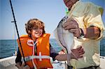 Boy and grandfather with caught fish on boat,  Falmouth, Massachusetts, USA