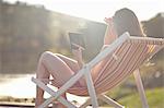 Young woman on deckchair using digital tablet