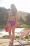 Young woman carrying flipflops on river pier