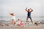 Parents and two young girls jumping mid air on beach