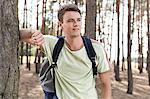 Happy young man with backpack hiking in woods