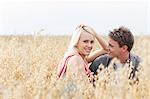 Portrait of beautiful young woman sitting with boyfriend amidst field
