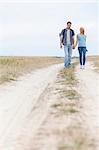 Full length of young hiking couple walking on trail at field