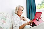 Senior woman using digital tablet while having coffee on bed at home