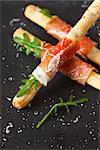 Bread sticks grissini with prosciutto ham and grated parmesan cheese.