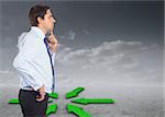 Thinking businessman touching his chin against green arrows in a desert landscape