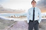 Smiling businessman standing with hand in pocket against rocky path leading to large urban sprawl