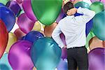 Thinking businessman scratching head against colourful balloons