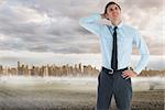 Thinking businessman with hand on head against large city on the horizon
