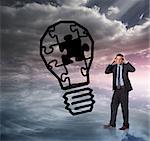 Stressed businessman with hands on head against light bulb graphic on colourful horizon