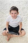 Smiling boy indoor. Sitting on the floor with tablet