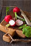 Fresh radish and old knife on wooden cutting board.
