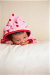 Portrait of two week old, newborn Asian baby girl in pink polka dot hooded jacket, studio shot on white background