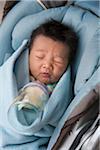 Close-up of swaddled two week old, newborn Asian baby girl, lying in car seat, disgusted with her milk bottle