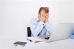 Tired businessman with hands on face sitting at desk by laptop