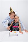 Portrait of happy father and daughter cutting birthday cake at table