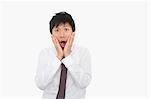 Shocked mid adult businessman with hands on face over white background