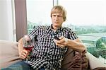 Displeased mid-adult man with wine glass watching television on sofa at home