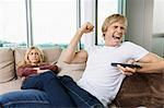 Angry woman staring at cheerful man as he watches TV in living room at home