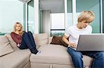 Sad woman beside man using laptop in living room at home