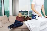 Man ironing shirt while woman sitting on sofa at home