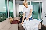 Man ironing shirt while woman relaxing on sofa at home