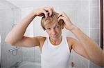 Portrait of man checking for white hair in bathroom