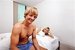 Portrait of man in underwear sitting on bed with woman looking at him