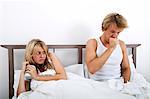 Scared woman looking at man coughing in bed