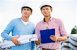 Architects with blueprint and clipboard standing at site