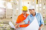 Male architects discussing over blueprint at construction site