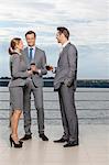 Full length of smiling businesspeople with wineglasses standing on terrace