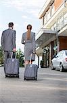 Back view of businesspeople walking with luggage outside hotel