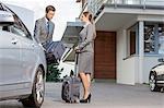 Businesspeople unloading luggage from car outside hotel