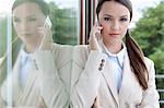 Portrait of confident businesswoman answering cell phone by glass door