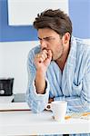 Young man coughing with coffee mug and medicine on kitchen counter