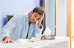 Young ill man with coffee mug, medicine and tissue leaning on kitchen counter