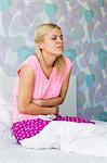 Young woman suffering from stomach pain in bedroom