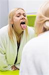 Young woman examining tongue in mirror