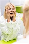 Young ill woman crying while looking at mirrior in bathroom