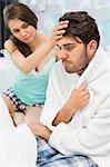 Young woman checking man's temperature on bed