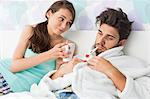 Young woman giving coffee mug to man with thermometer in mouth