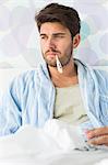 Sick man with thermometer in mouth sitting on bed