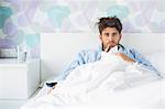 Portrait of sick man with thermometer in mouth reclining on bed at home