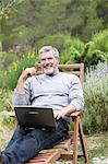 Man sitting in his garden with laptop, smiling