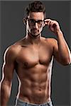 Shirtless male model posing with glasses over a gray background