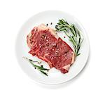 Raw sirloin steak with rosemary and spices on plate. Isolated on white background