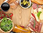 Red wine with cheese, olives, tomatoes, prosciutto, bread and spices. Over wooden table background. View from above with copy space