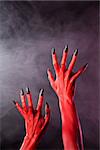 Red devil hands with sharp black nails, Halloween theme, studio shot over smoky background